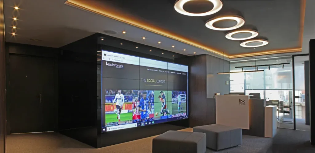 Zona de espera con videowall, pufs grises y techo con aros luminosos en las oficinas de Leaderbrock, Valencia